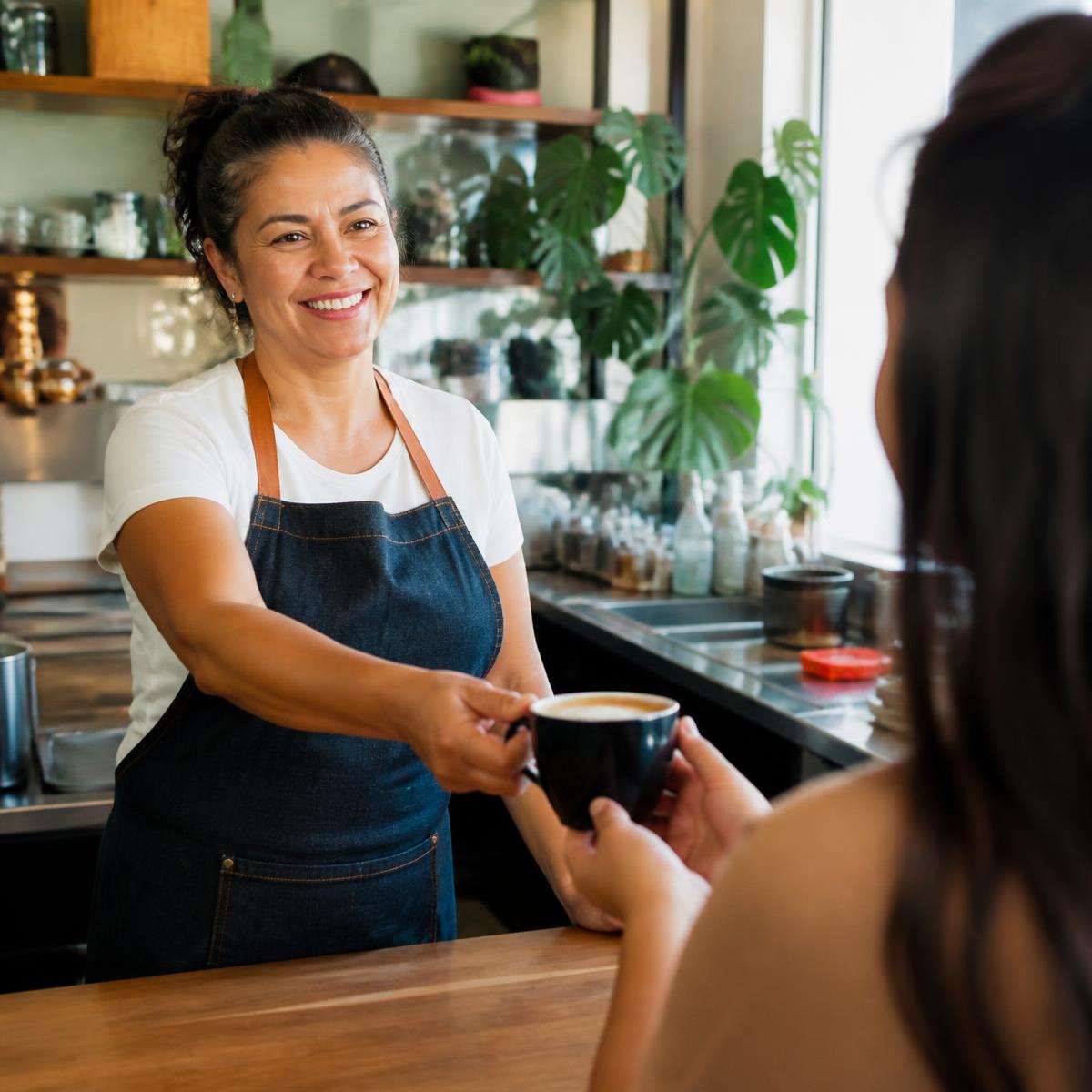 Proprietária de cafeteria entregando um café para uma cliente no balcão